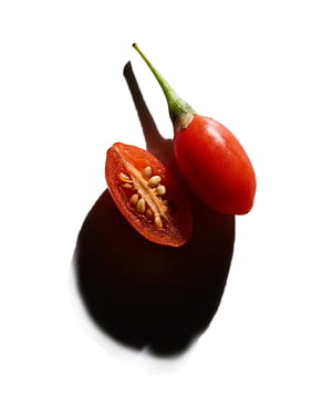 One whole goji berry and one sliced in half showing the seeds, on a white background.