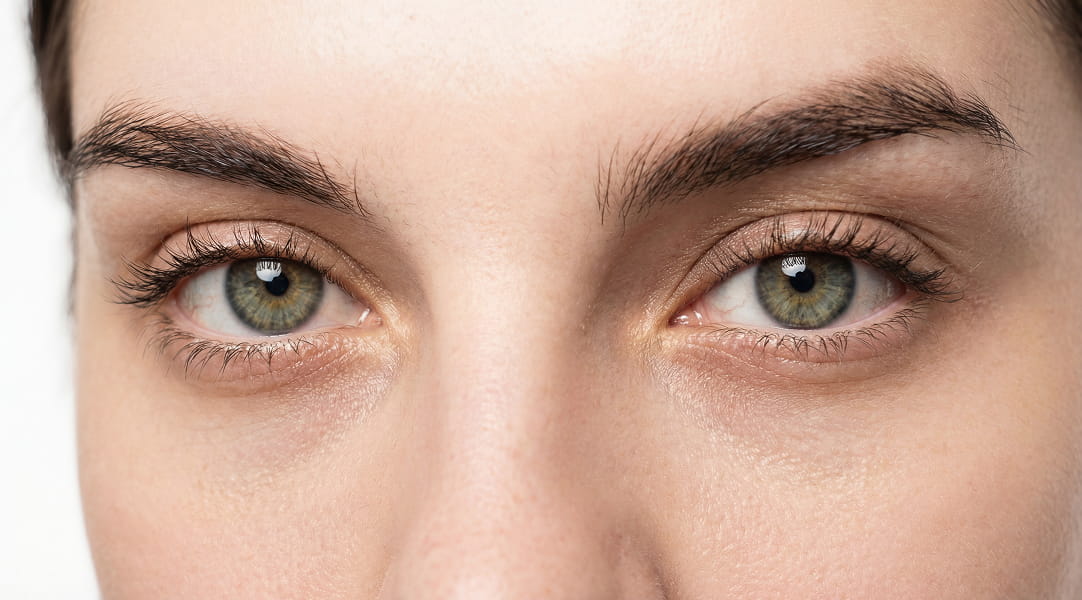 A close-up of a person's green eyes with dark eyebrows, looking straight ahead.