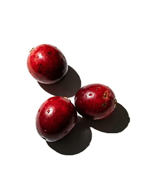 Three shiny red cranberries on a white background casting dark shadows.