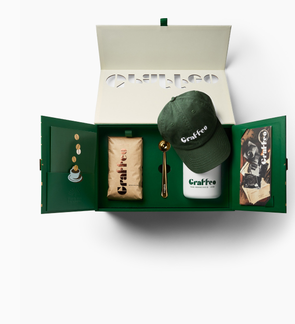 An open green Graffeo gift box containing a hat, tumbler, coffee, and a scoop against a white background.