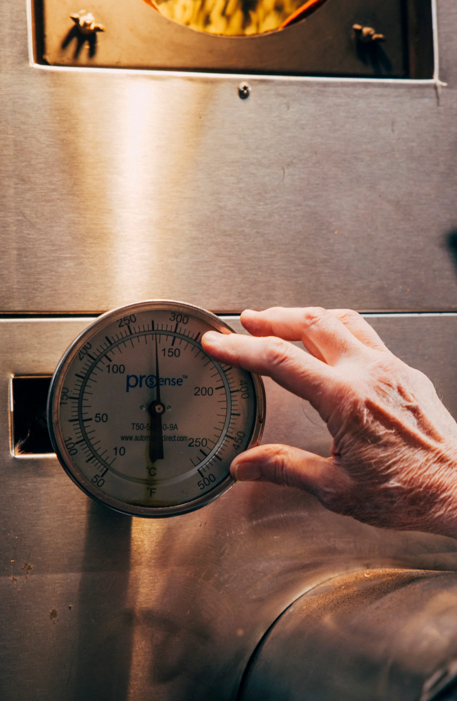 Hand adjusting a large dial thermometer on a metal surface.