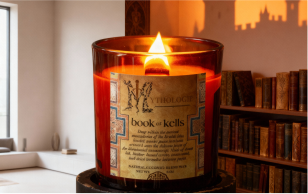 A lit candle in a glass holder labeled 'Book of Kells' with bookshelves in the background.