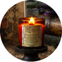 Lit candle on a black stand with decorative label and background items.