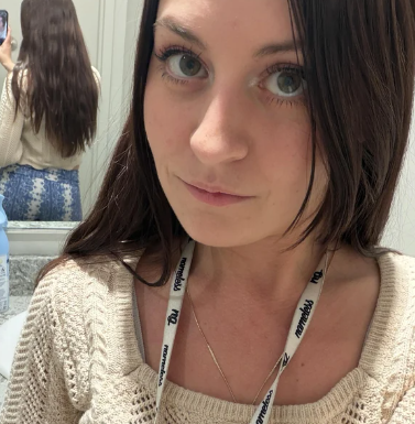 A woman with long brown hair takes a selfie in front of a mirror wearing a cream sweater.