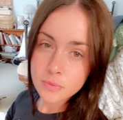 A close-up photo of a woman with long brown hair and hazel eyes looking at the camera.
