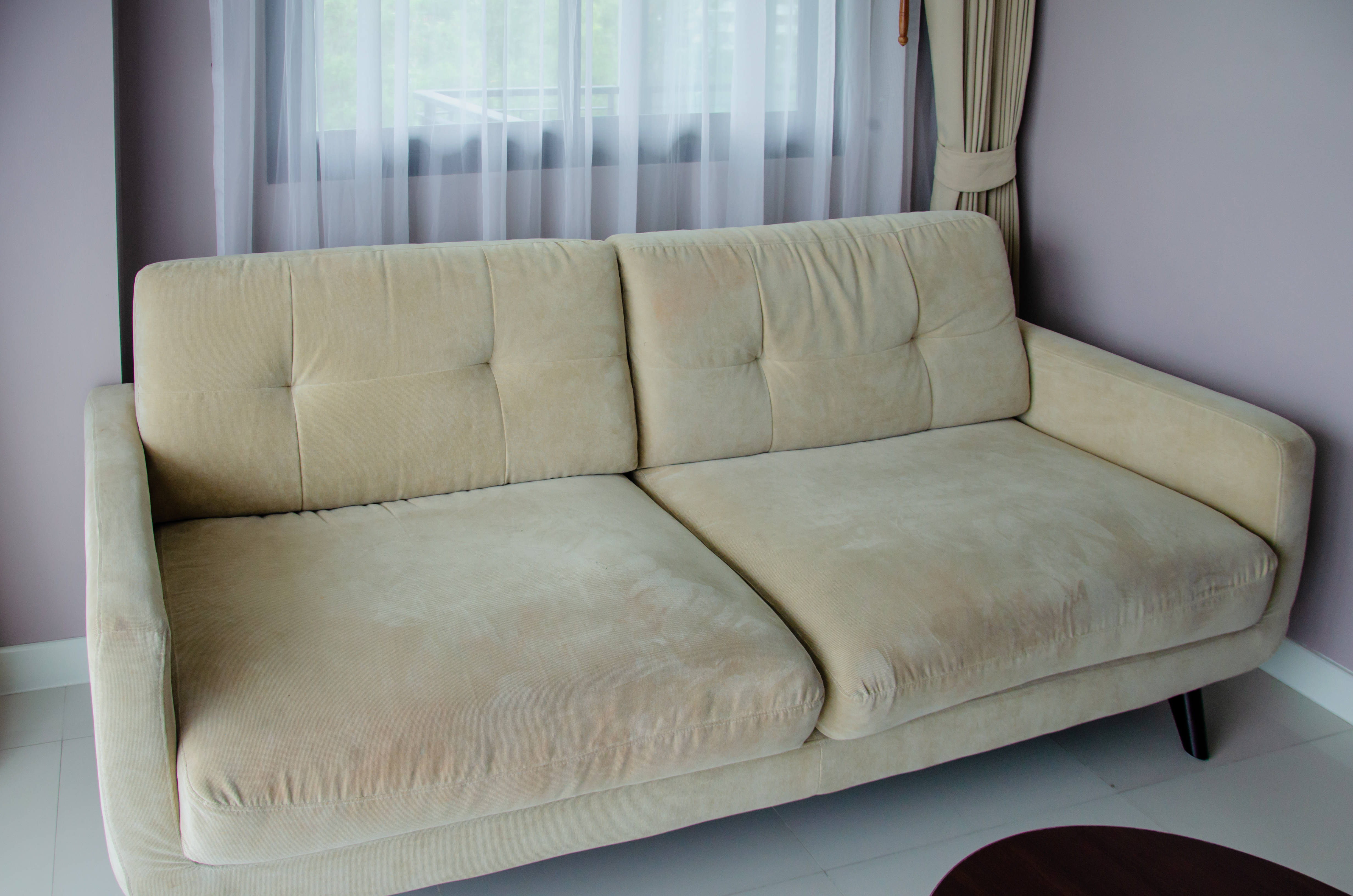 A beige sofa in a room with a window and curtains.