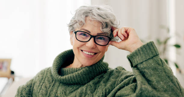 A smiling older woman with short gray hair and glasses, wearing a green cable-knit turtleneck sweater.