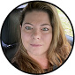 A woman with long hair sitting in a car, looking at the camera.