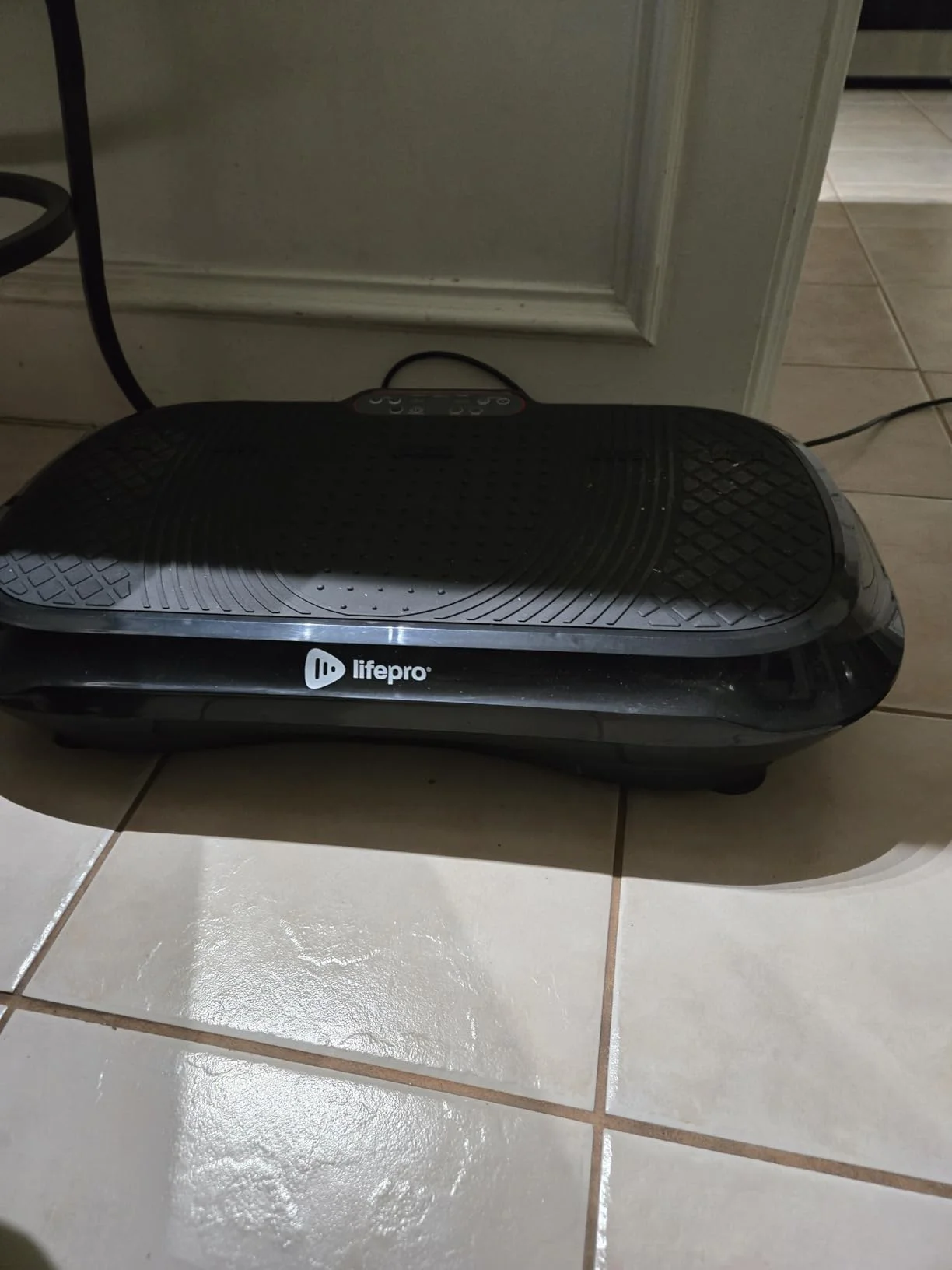 A black Lifepro vibration plate on a tiled floor indoors.