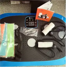 A blue and black exercise vibration plate with accessories including resistance bands, handles, and a manual.