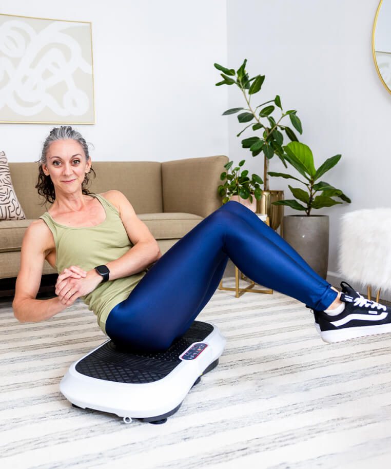 Woman exercising on a vibration plate in a living room.