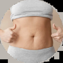 A woman in a grey top and underwear gives a thumbs-up to her stomach with stretch marks.