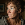 A low-resolution, pixelated close-up of a person with curly brown hair, looking to the side.