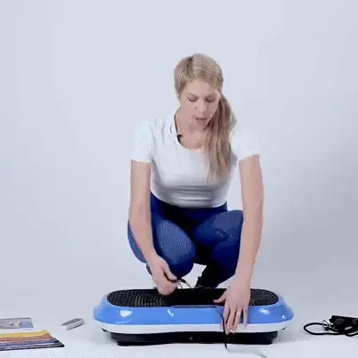Person assembling a blue vibration plate with accessories on the floor.