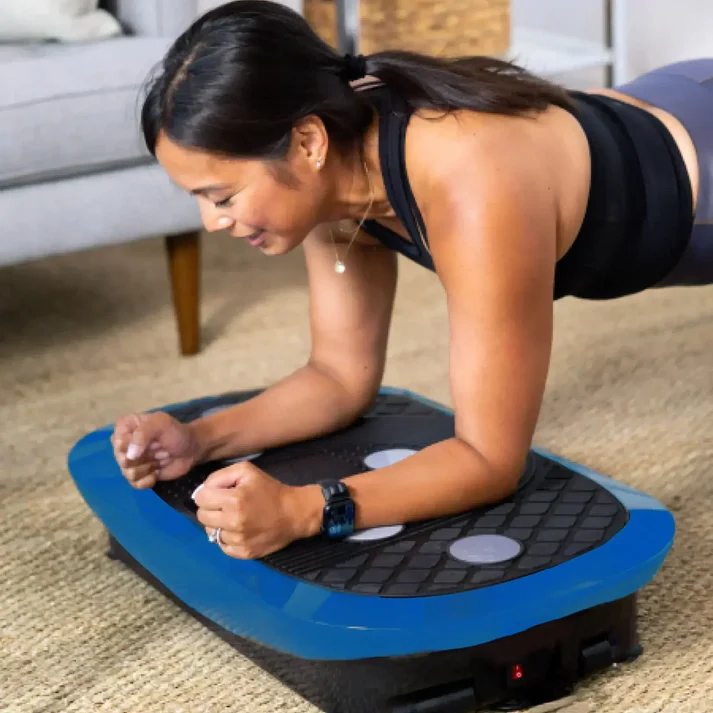 Person planking on a blue vibration plate in a living room.