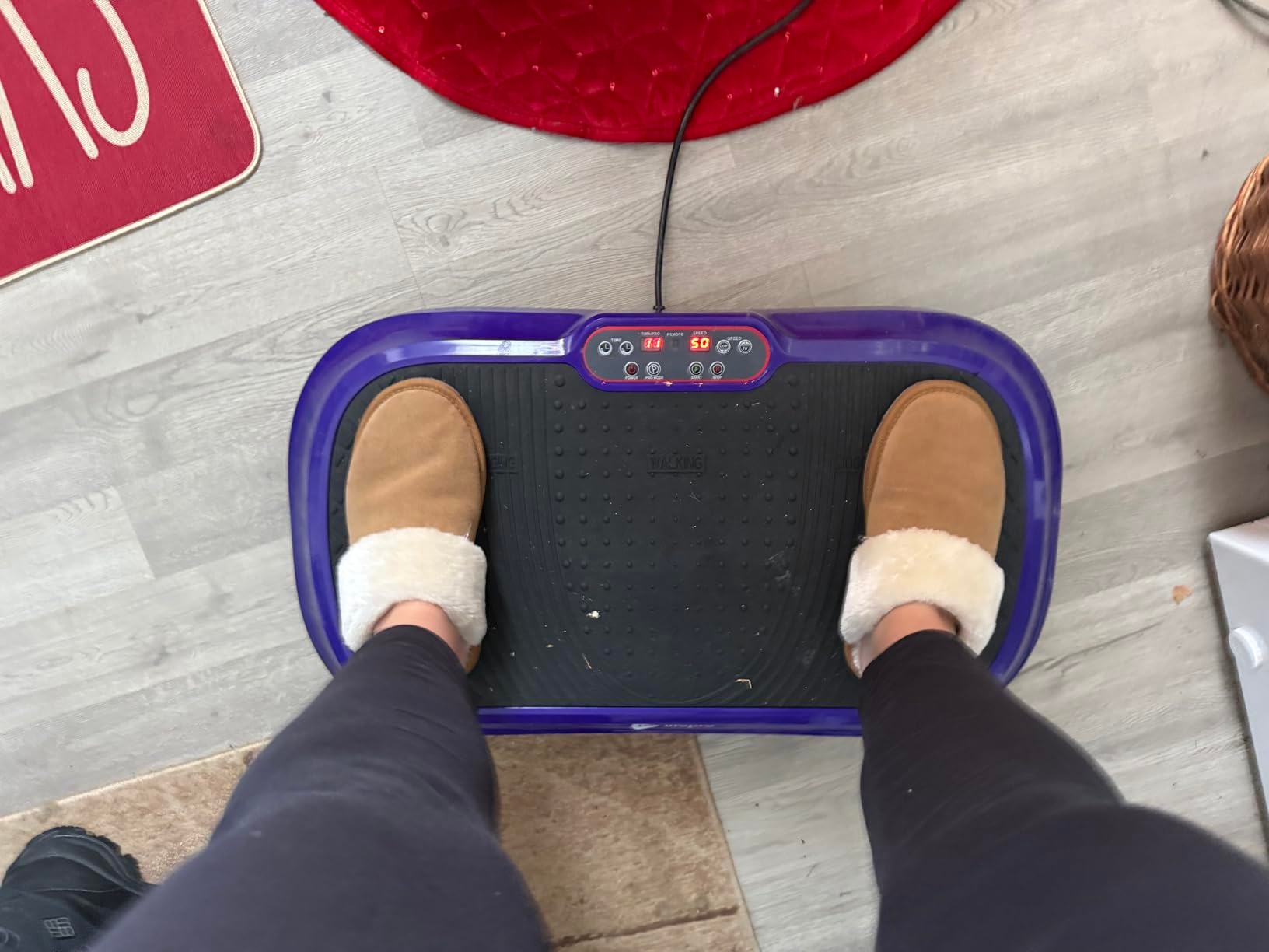 A person wearing fuzzy slippers stands on a purple vibration plate exercise machine.