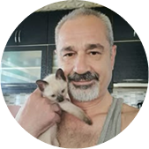 A man with a salt-and-pepper goatee holding a small, light-colored kitten.
