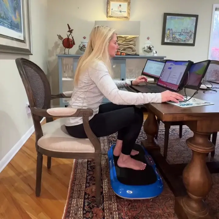 Person working on laptops at a table, feet on a blue balance board.