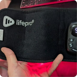 A hand holding a black Lifepro therapy belt with a red light glowing from within.