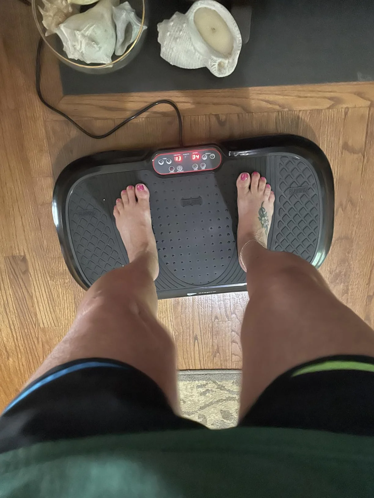 Person standing on a vibration platform with seashells nearby on a wooden floor.
