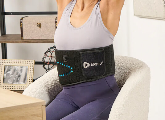 A person sits in a chair wearing a black Lifepro waist belt with blue lights.