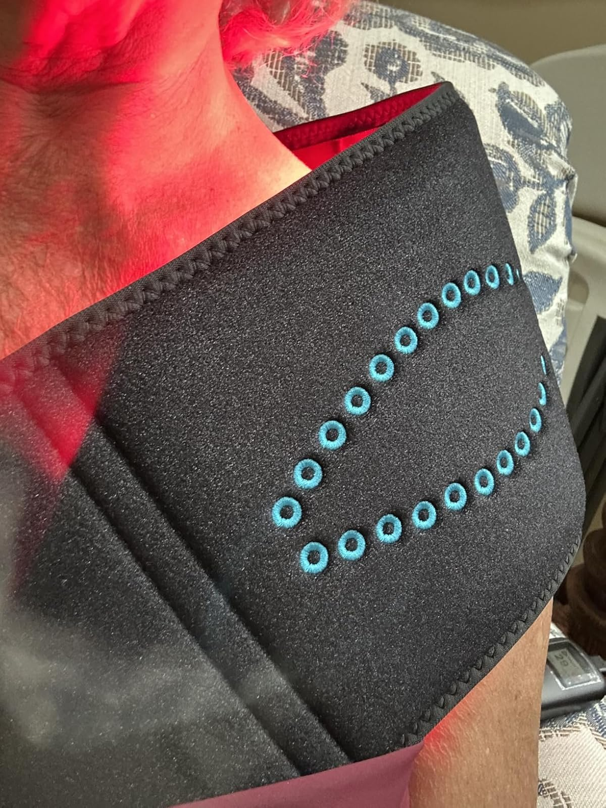 A person wears a black wrap on their shoulder and neck which glows with red light.