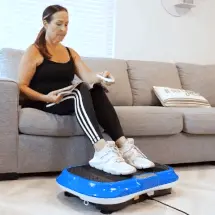 Woman sitting on a couch using a blue vibration platform.