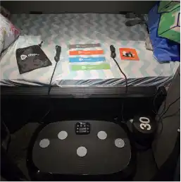 A vibration plate exercise machine with resistance bands and accessories displayed on a bed.