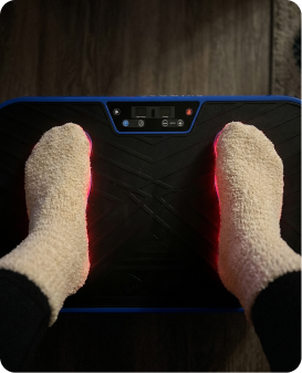 A person wearing fuzzy socks stands on a vibrating exercise platform with a digital display and red lights.