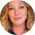 A circular, cropped headshot of a woman with wavy blonde hair and a tattoo on her forehead.