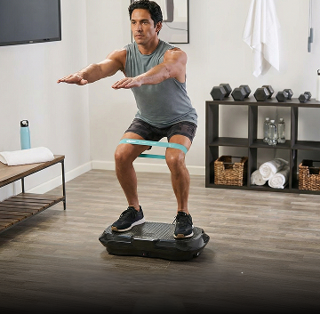 A man performs a squat on an exercise platform with a resistance band around his thighs.