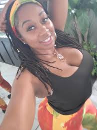 Smiling woman with dreadlocks wearing a colorful headband and outfit, posing indoors.
