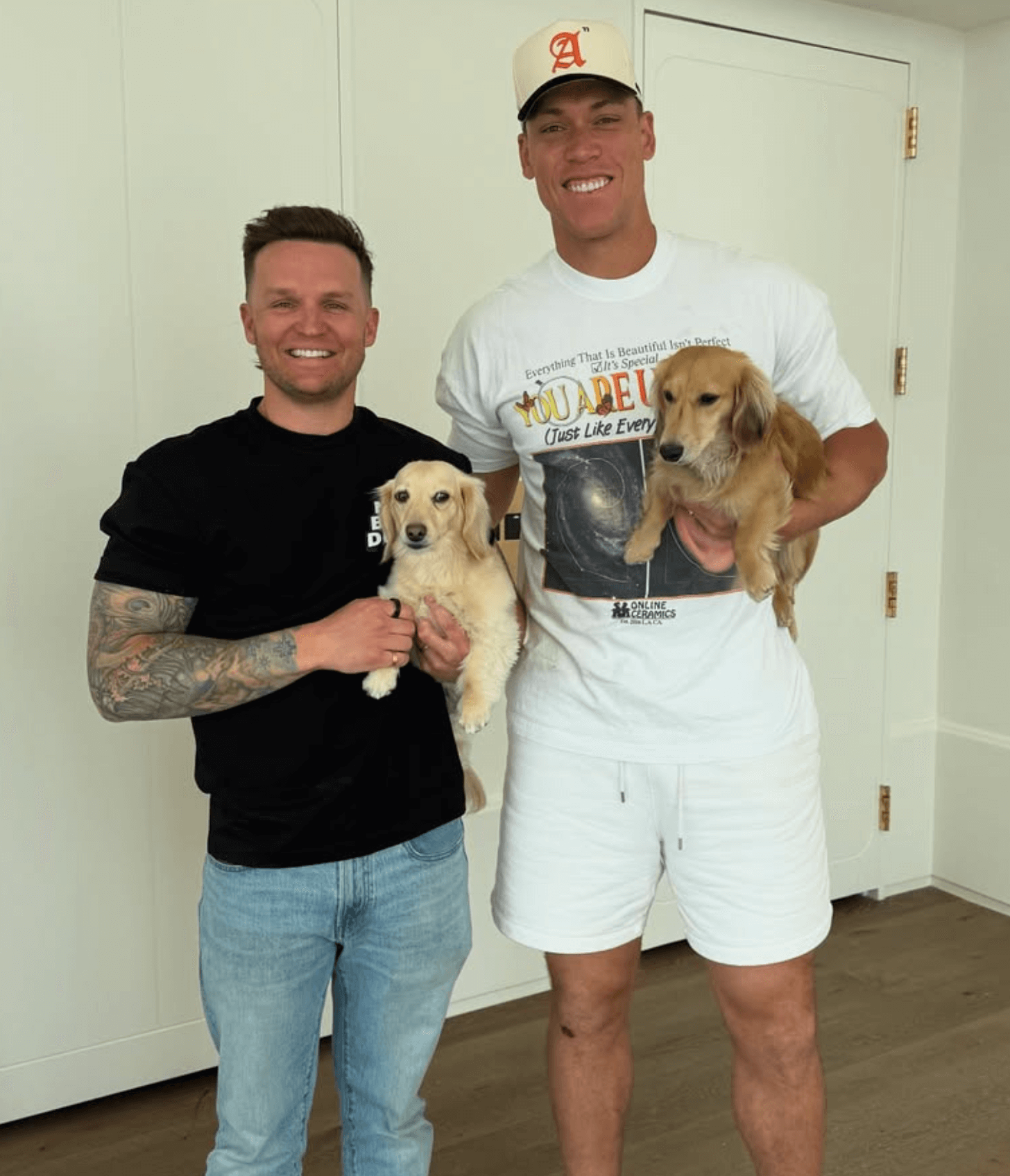 Two men smiling, each holding a small dog indoors.