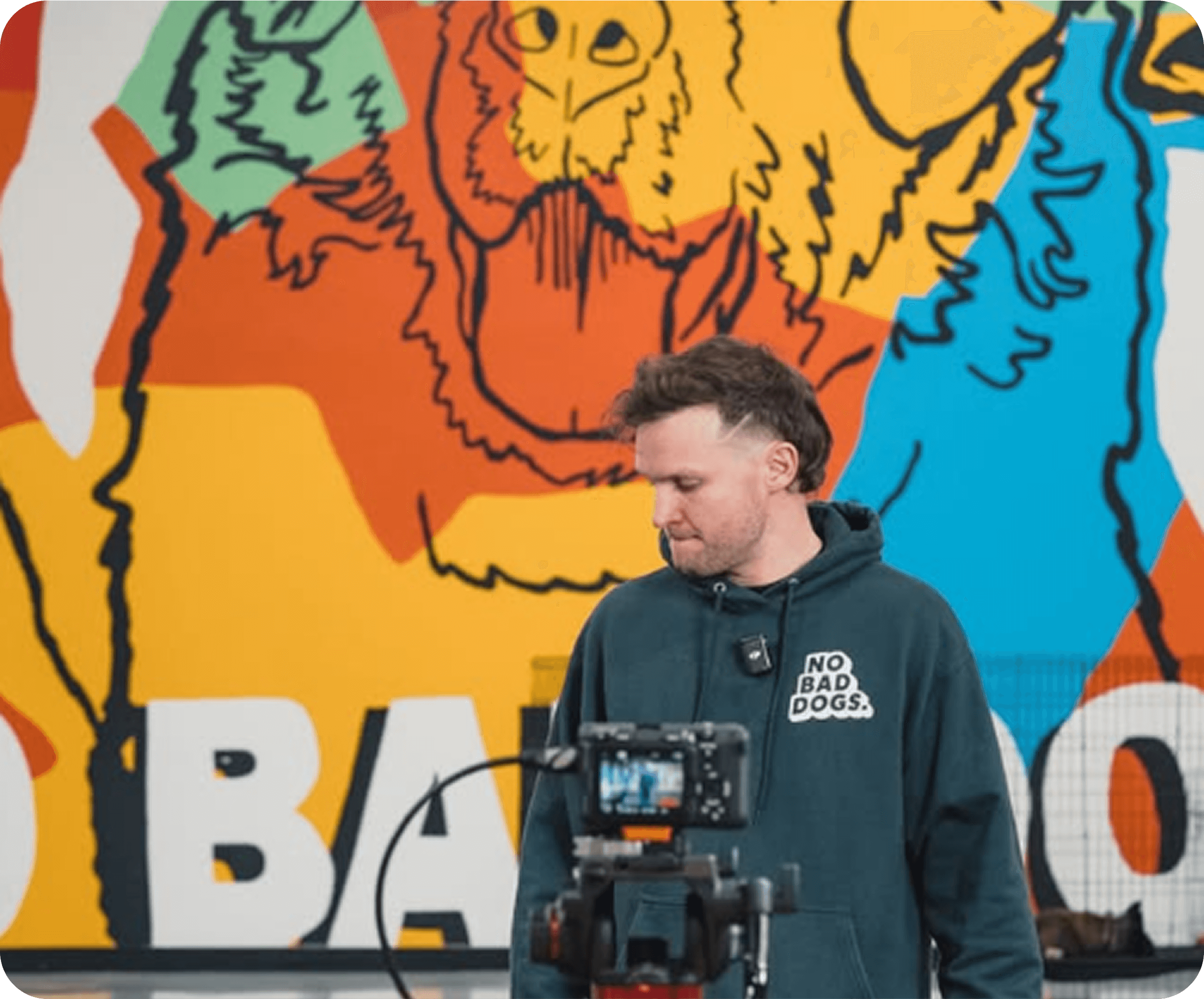 Person in front of colorful mural with camera on tripod.