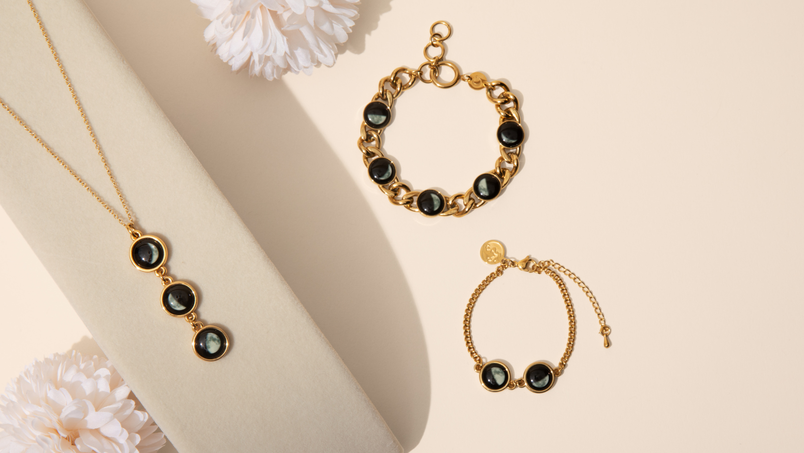 Gold necklace and bracelets with black stones on a beige background.
