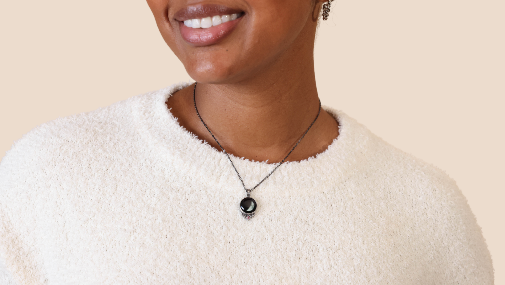 Person wearing a white sweater and a pendant necklace.