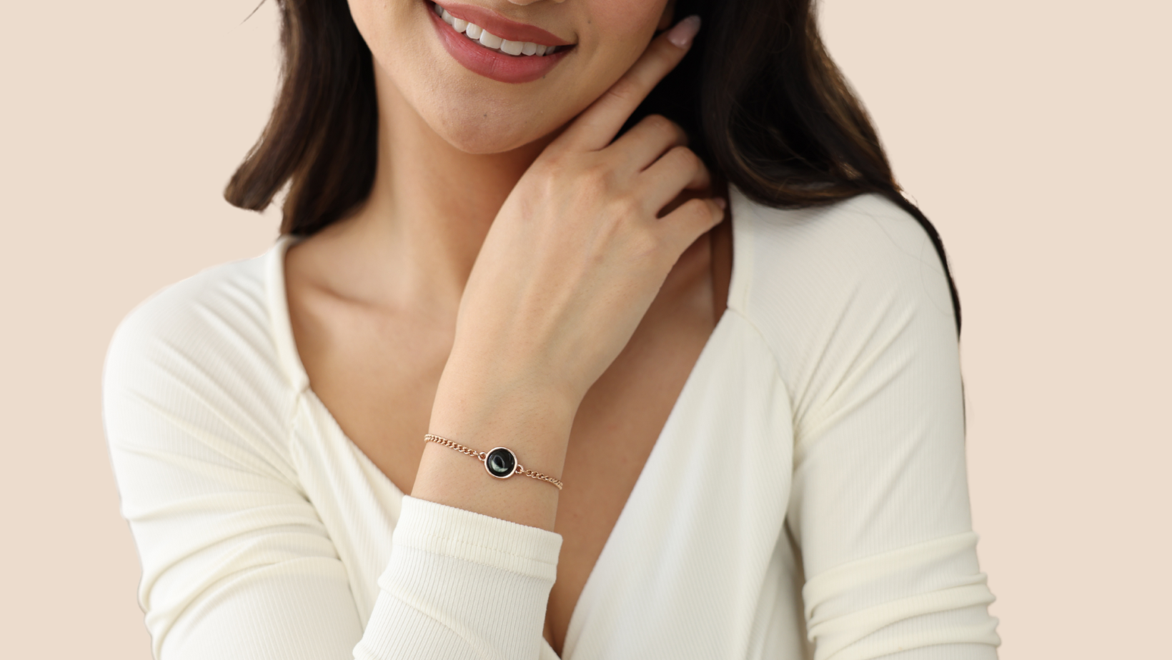 Woman wearing a bracelet, smiling, with hand near face.