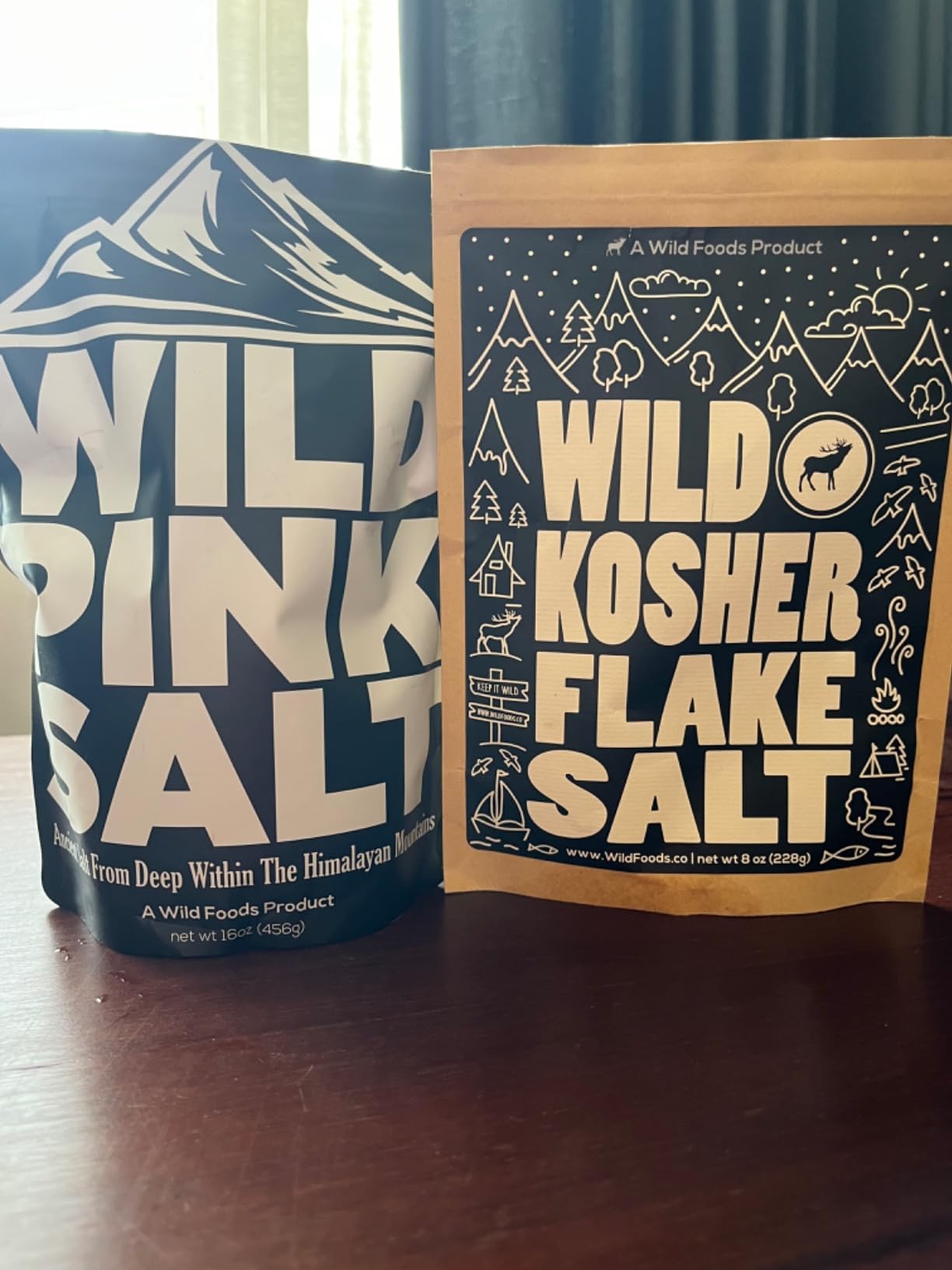 A bag of Wild Pink Salt next to a bag of Wild Kosher Flake Salt on a table.