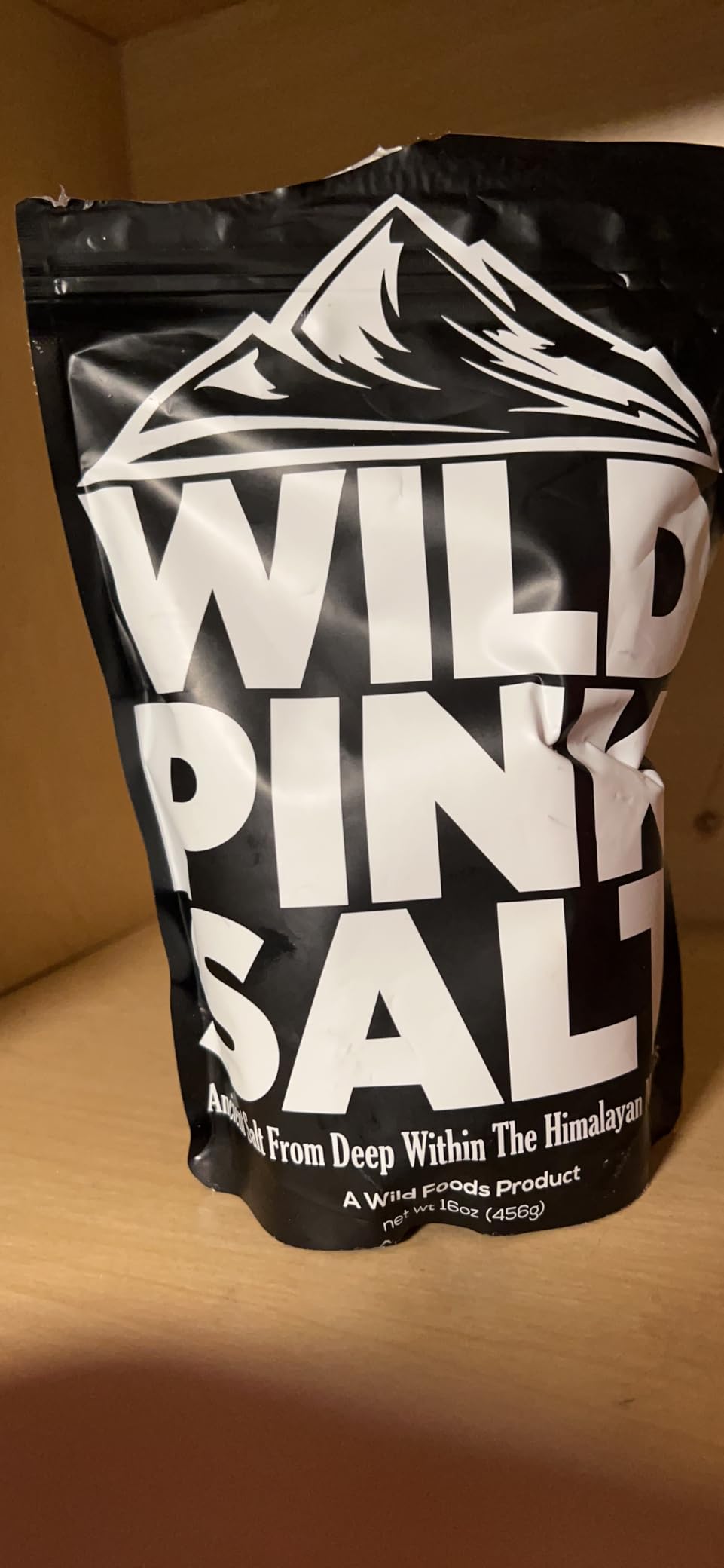 A black bag of Wild Pink Salt from Wild Foods sitting on a wooden shelf.
