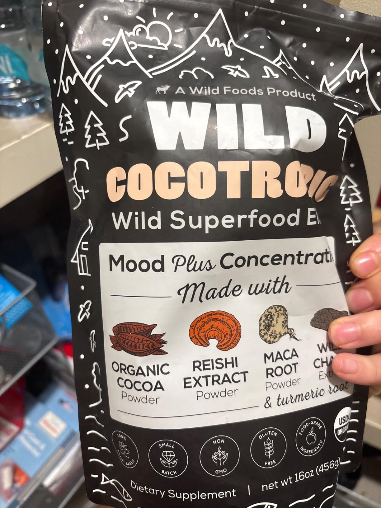 A hand holds a black pouch of Wild Cocotropic Wild Superfood Elixir dietary supplement.