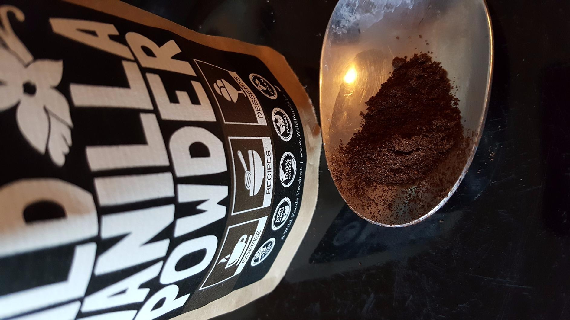 A paper bag lies next to a spoon filled with a dark brown powder on a black surface.