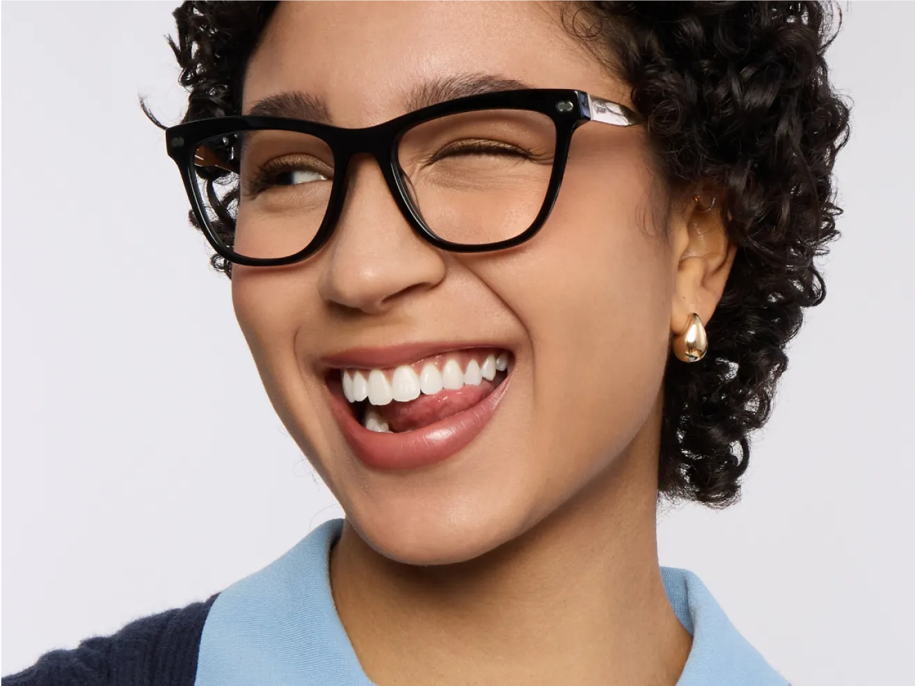 Person winking and smiling, wearing glasses and earrings.