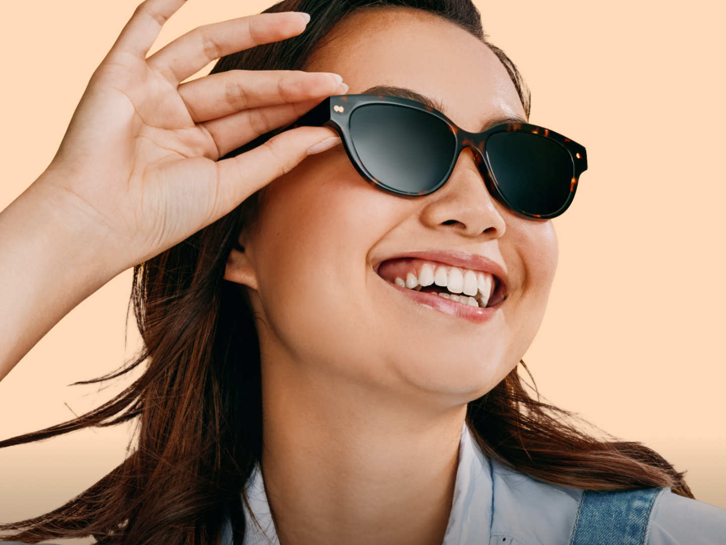 Smiling person wearing sunglasses against a peach background.