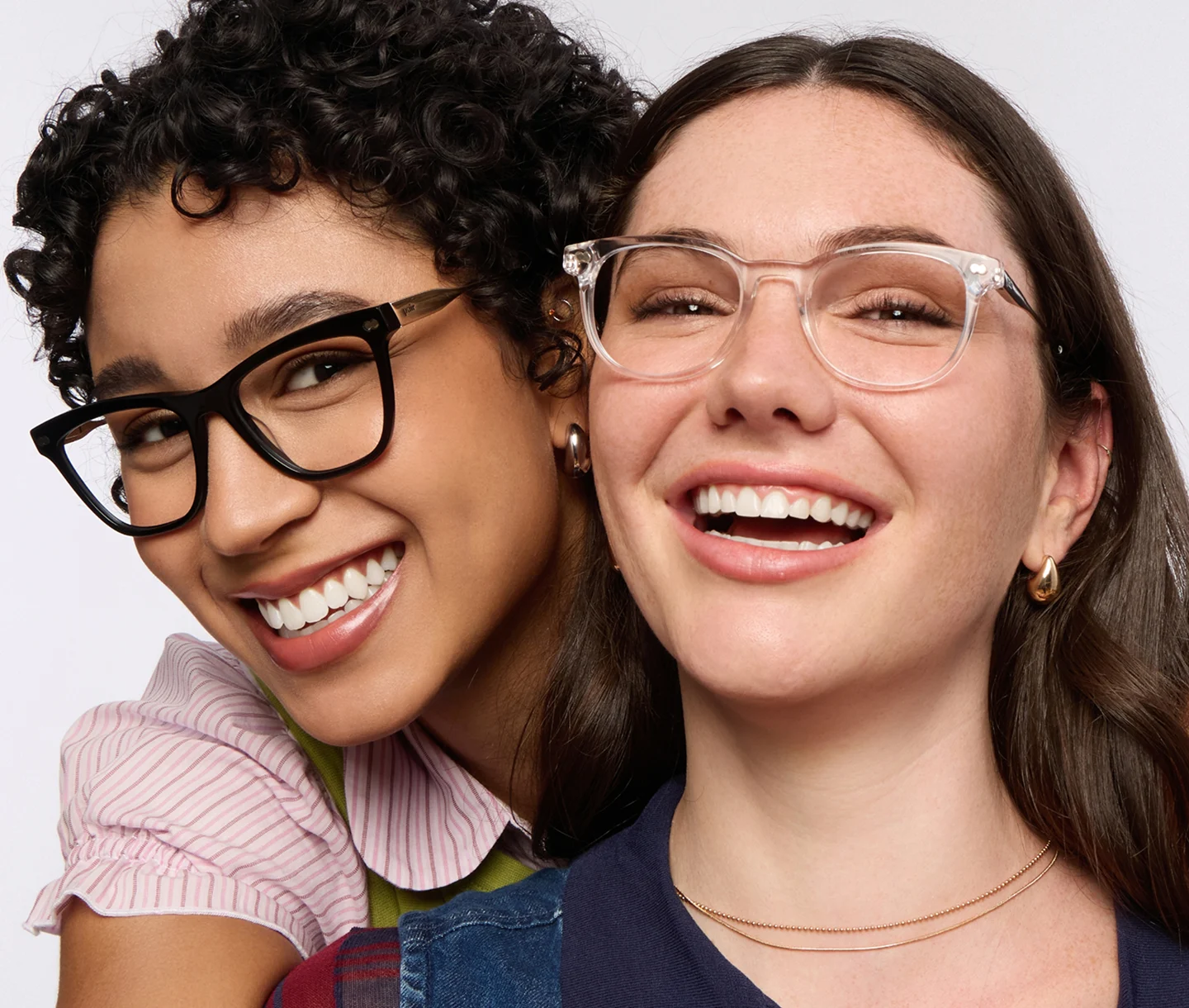 A close-up of two smiling women, both wearing glasses against a white background.
