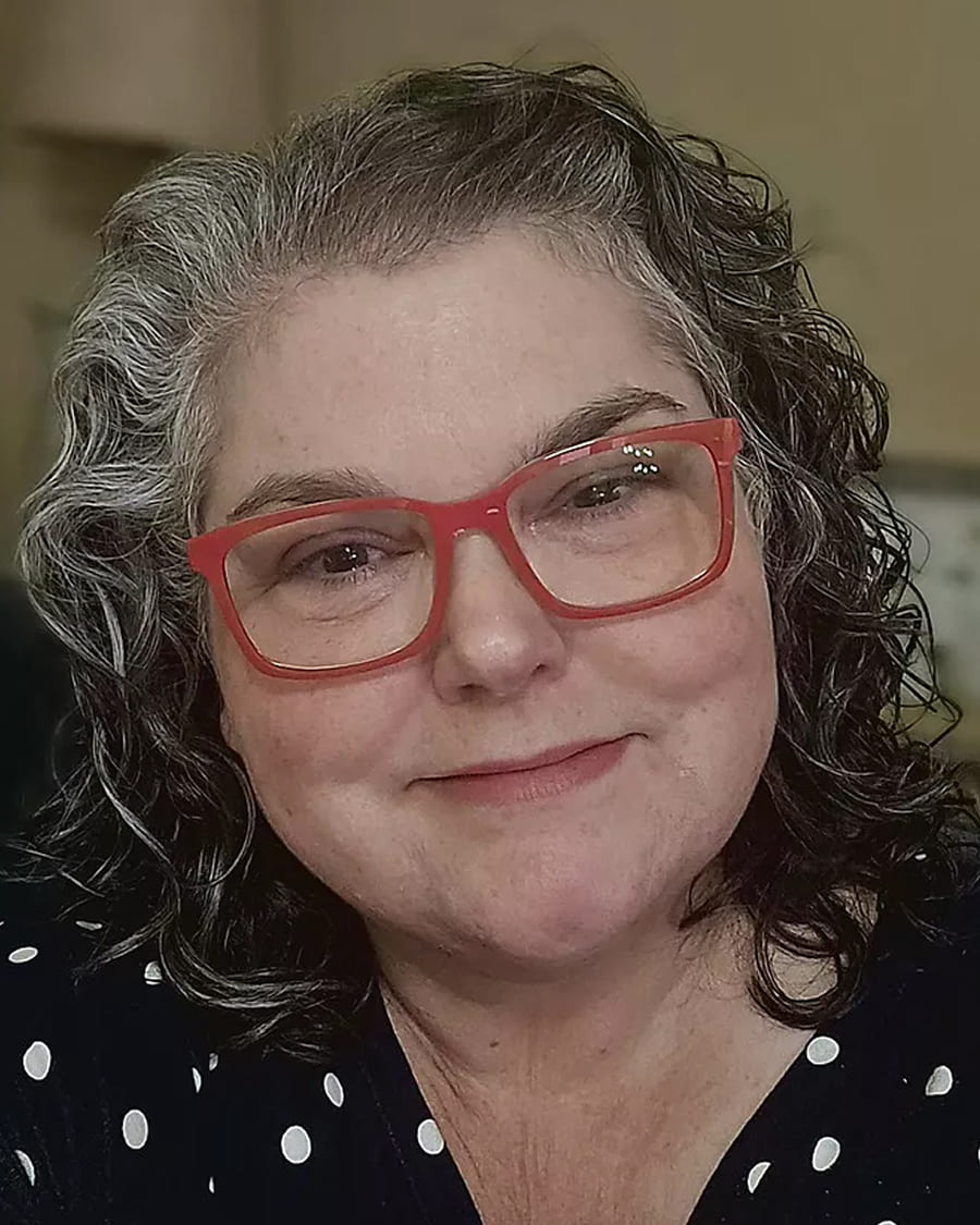 Person with curly hair and red glasses smiling at the camera.