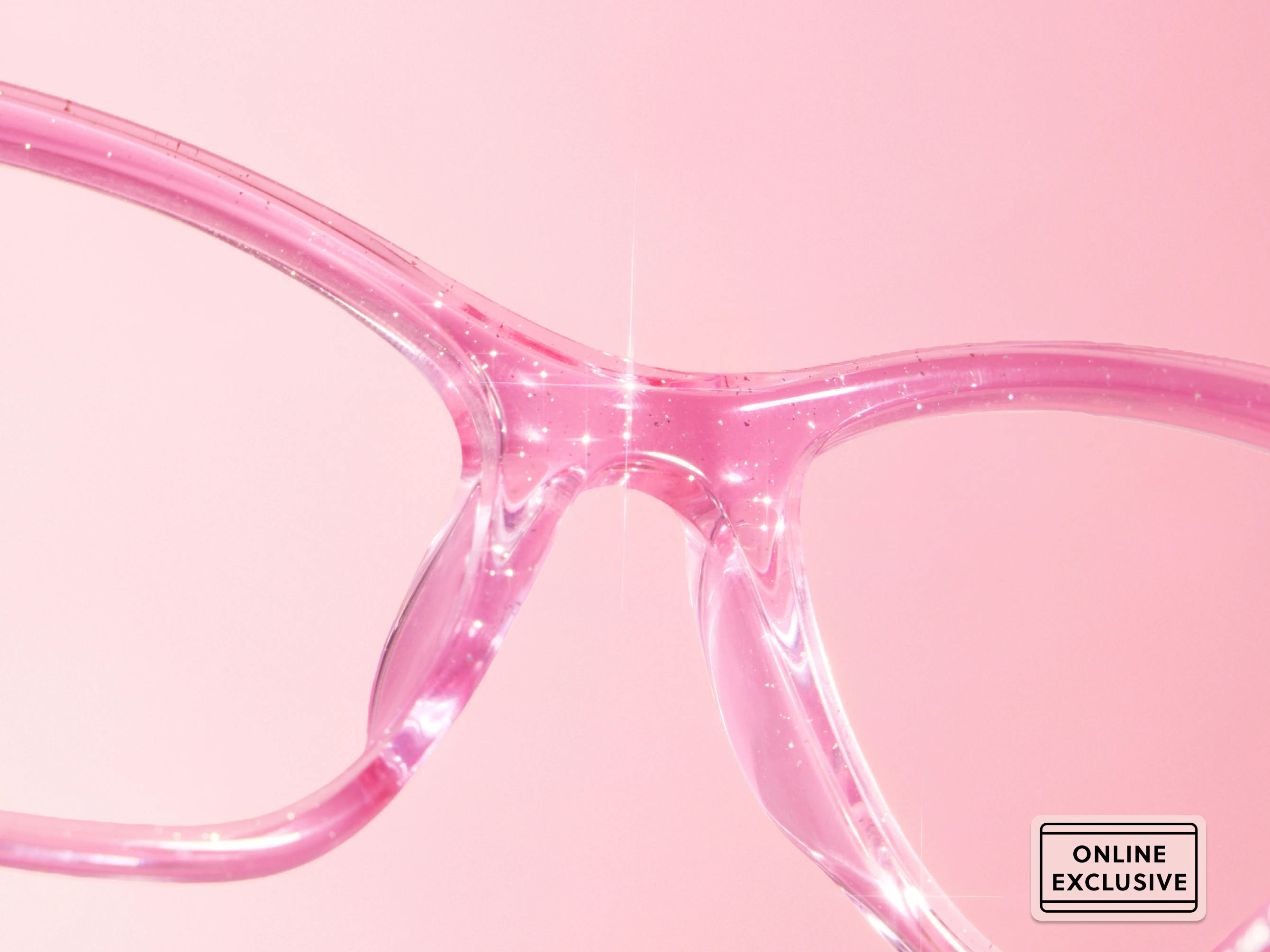 Close-up of pink translucent eyeglass frames with glitter, labeled 'online exclusive'.