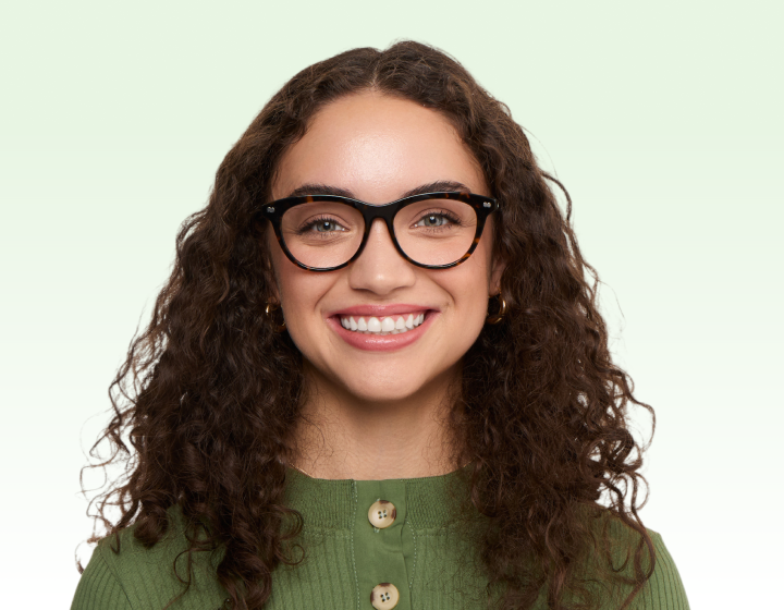 A smiling woman with long curly brown hair, wearing tortoiseshell glasses and a green top.