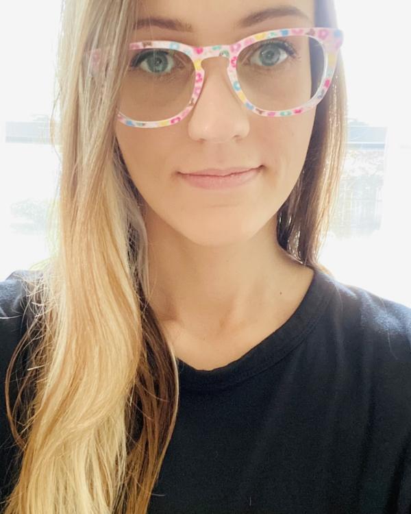 Person wearing colorful glasses and a black shirt, smiling slightly.