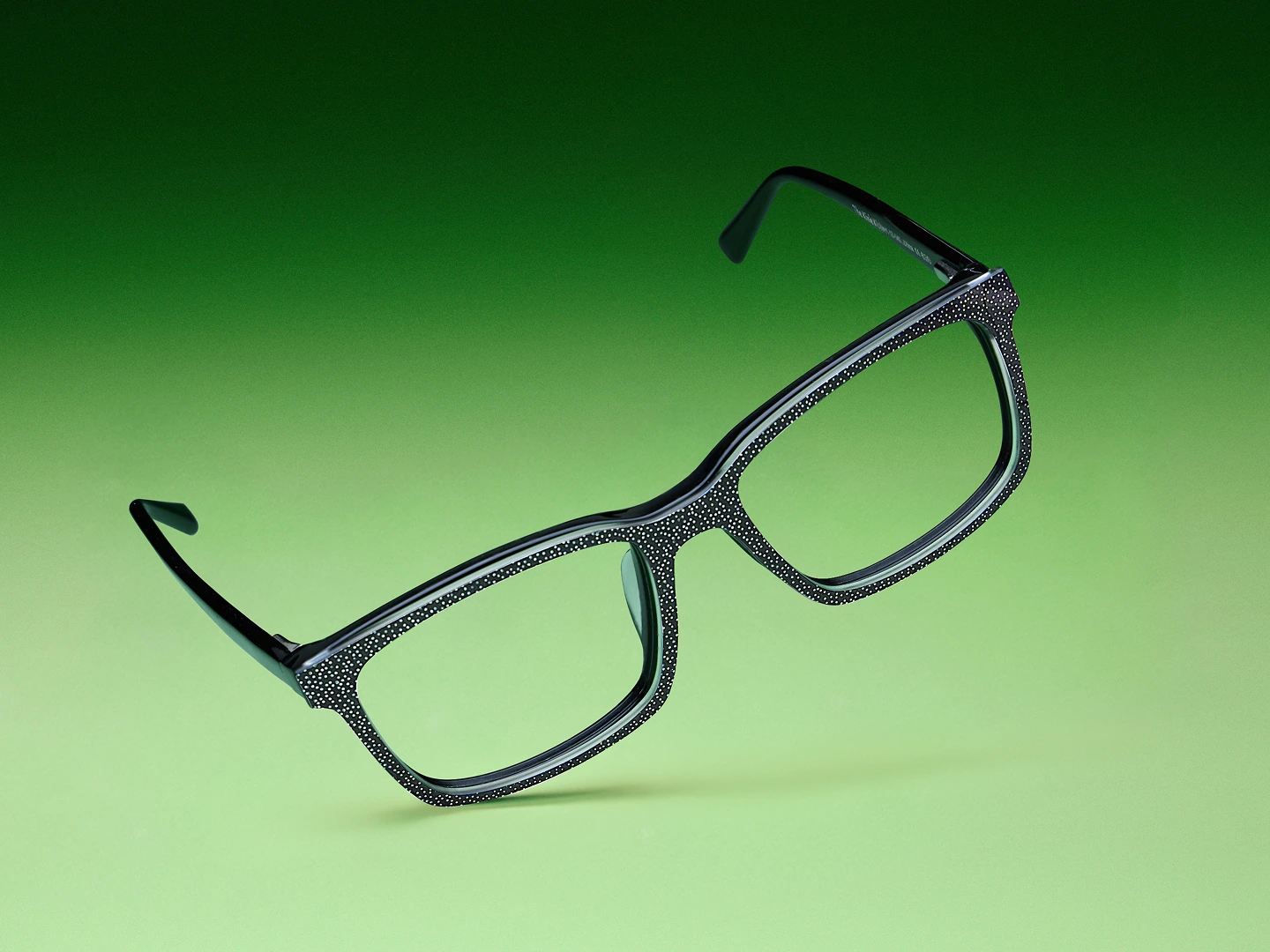 Black eyeglasses with a dotted design on a green background.