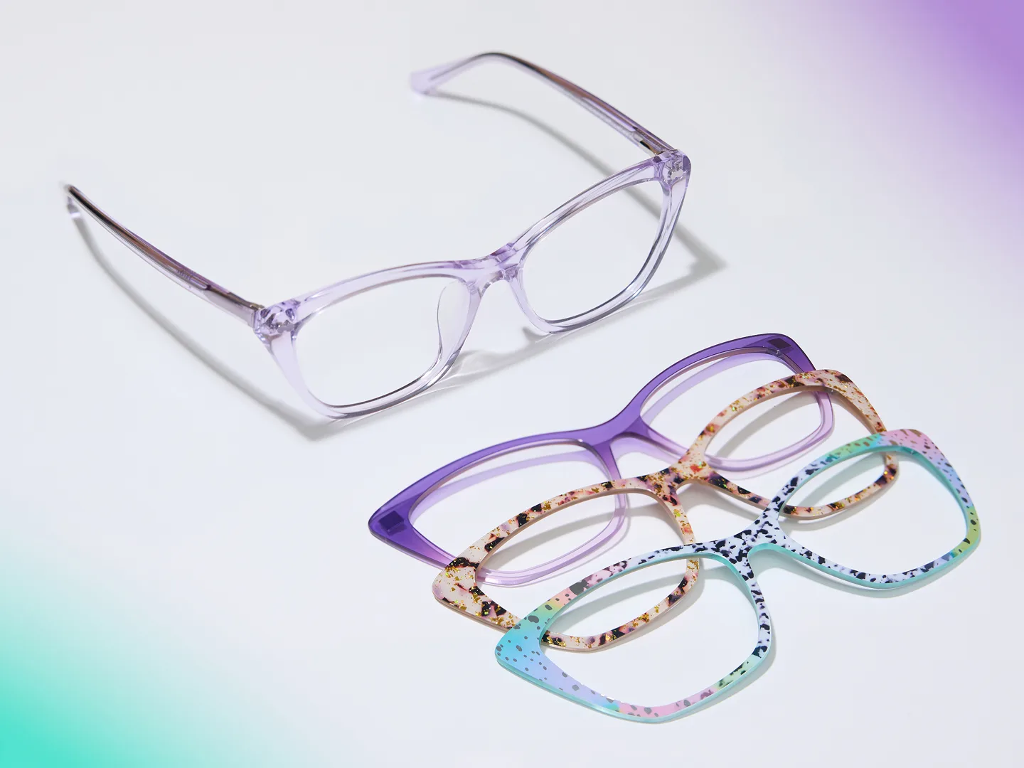 A pair of light purple eyeglasses and three colorful, patterned eyeglass frames on a white and purple surface.